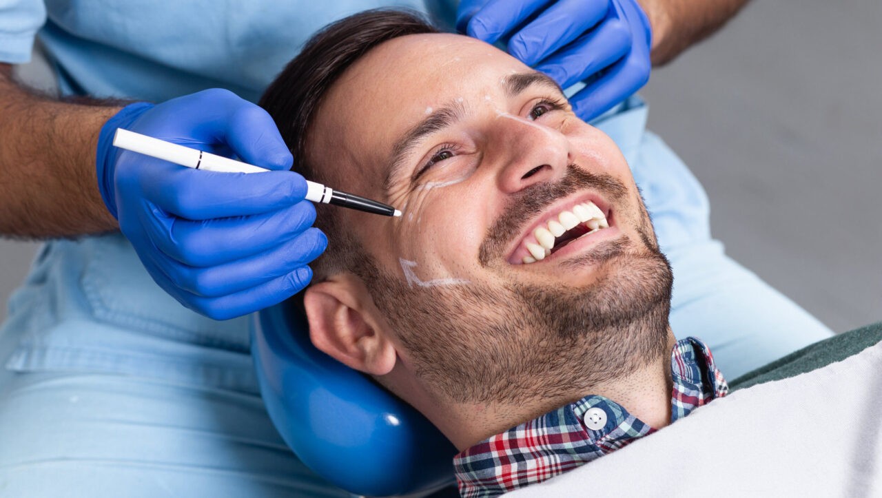 Happy male patient with correction lines on the face in an examination room.