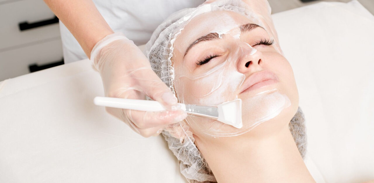 Cosmetologist in gloves holds cosmetic brush for applying mask