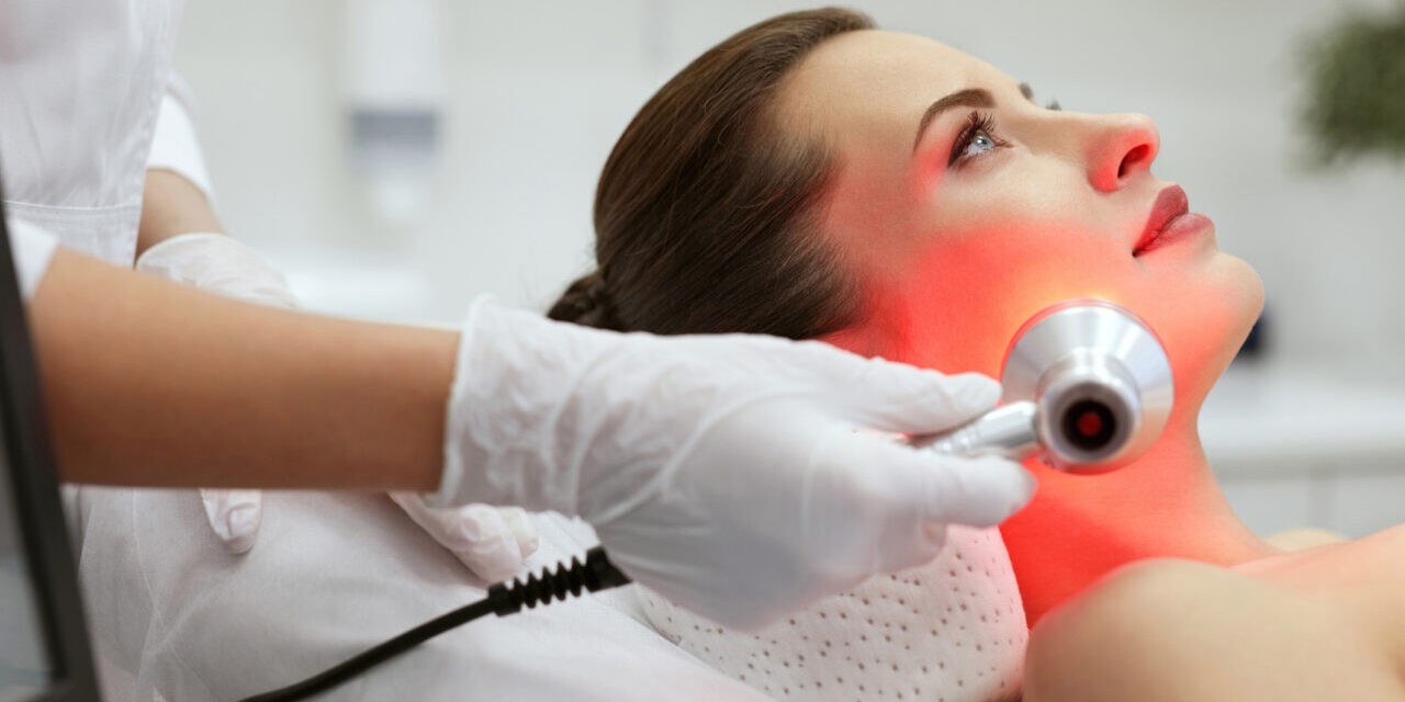 Facial Beauty Treatment. Woman Doing Red Led Light Therapy On Face Skin At Cosmetology Center. High Resolution