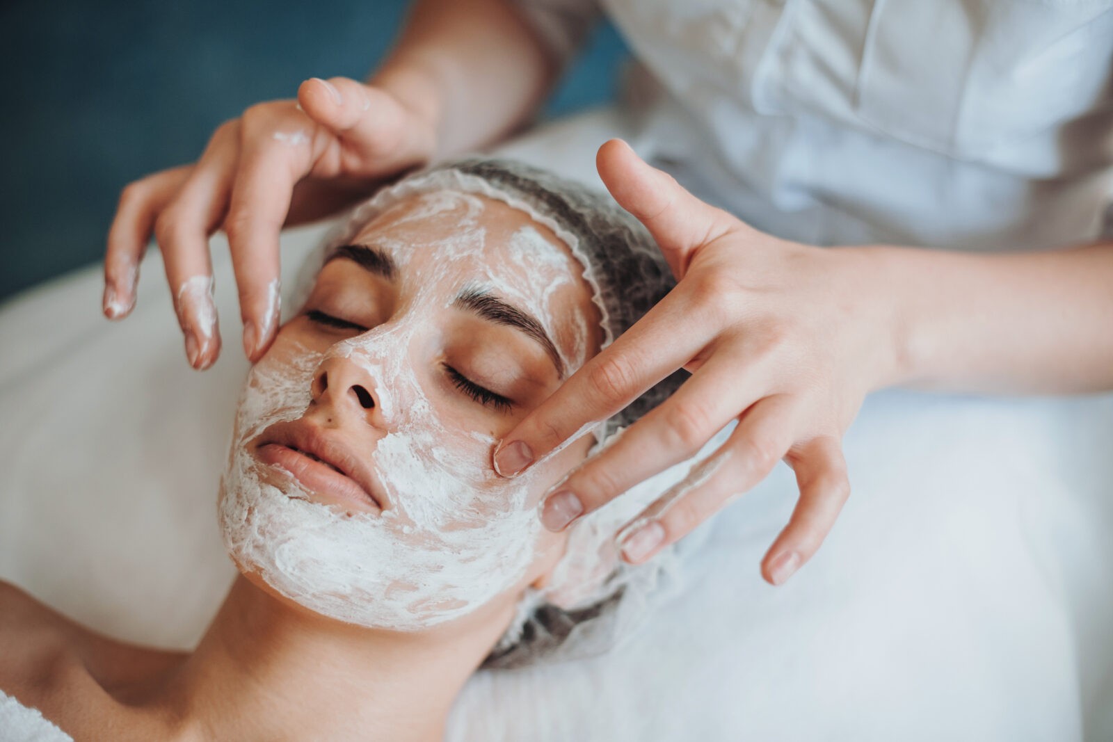 Closeup of a cosmetologist applying mask on client's face in spa salon.