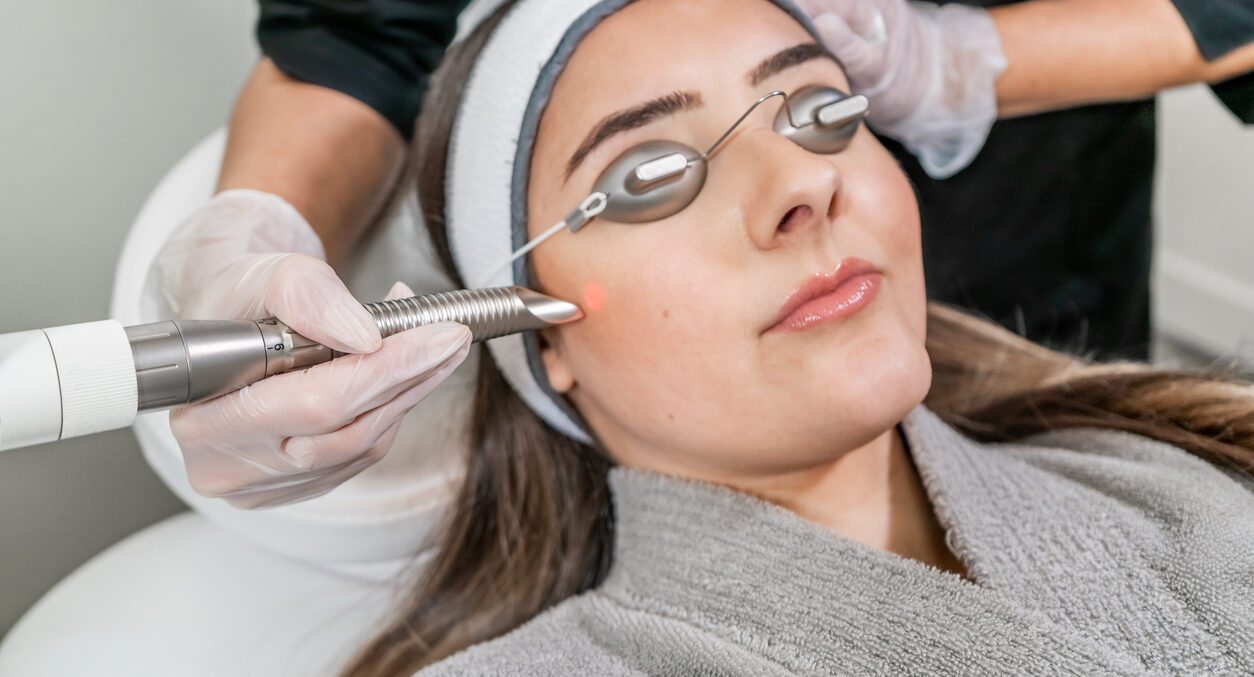 Beauty technician dermatologist performing a cosmetic laser treatment on a female patient.