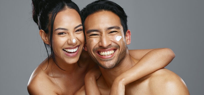 Couple, smile and love for skincare, care and portrait with moisturizer in studio by gray background. Happy people, dermatology and hug for cosmetics, hydration and creme or love for skin treatment